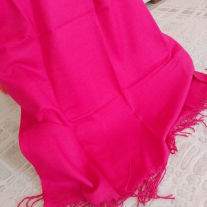 May include: A bright pink shawl with fringe detailing. The shawl is made of a soft, lightweight fabric.