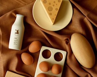 May include: A wooden toy set featuring a white milk bottle with a cow graphic, a wedge of Swiss cheese on a plate, a loaf of bread, four brown eggs in a wooden carton, and a rectangular butter block labeled BUTTER with a cow illustration.