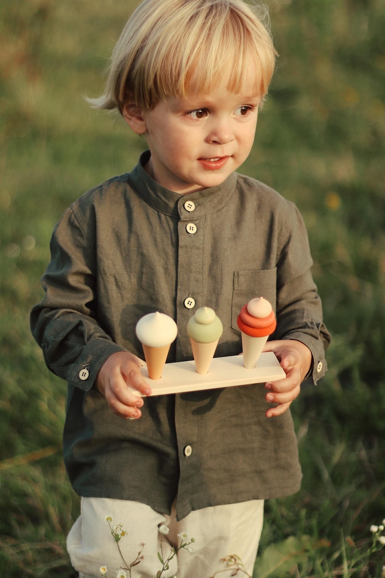 Toddler holding a wooden ice cream toy set with three pastel cones — Montessori pretend play food.