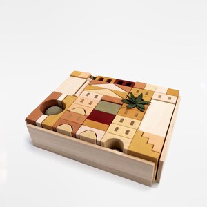 May include: A wooden toy set with a variety of blocks in different shapes and sizes. The blocks are arranged in a tower formation and include a small green plant. The blocks are in shades of brown, beige, and yellow.