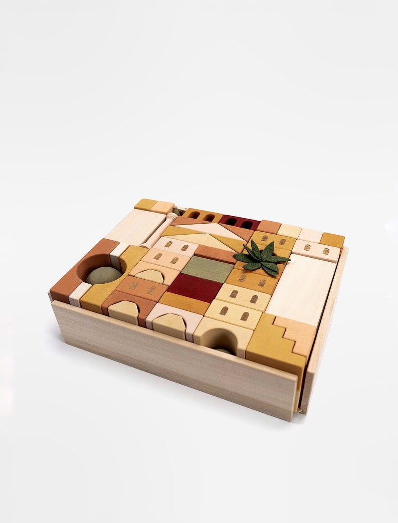 May include: A wooden toy set with a variety of blocks in different shapes and sizes. The blocks are arranged in a tower formation and include a small green plant. The blocks are in shades of brown, beige, and yellow.