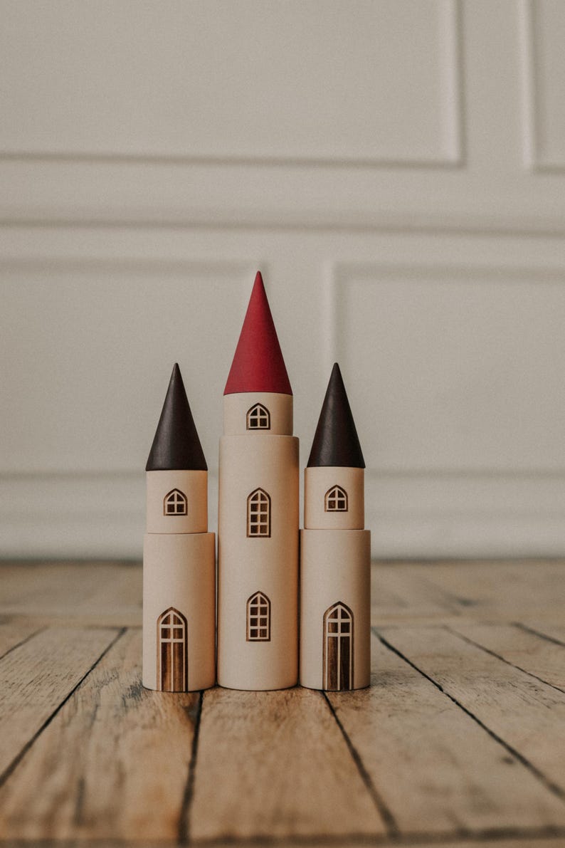 Puede incluir: Tres torres de juguete de madera con techos rojos, negros y marrones. Las torres est&aacute;n apiladas en un suelo de madera.
