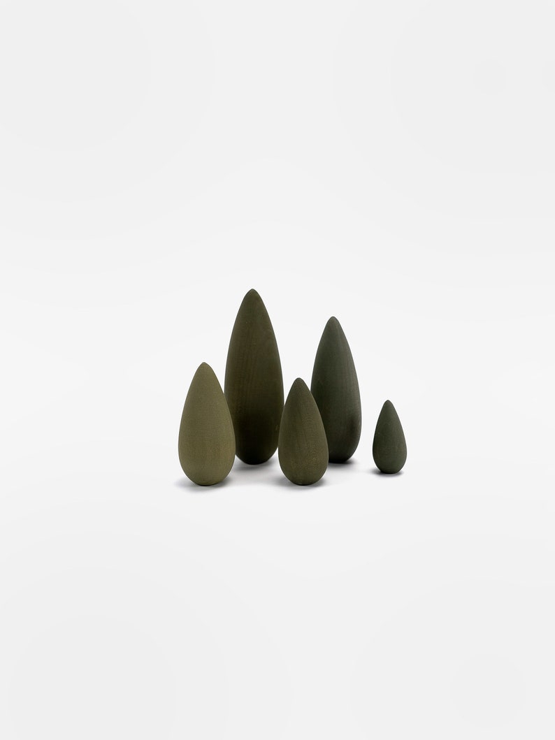 May include: A set of five wooden teardrop-shaped ornaments in shades of green. The ornaments are arranged in a staggered formation, with the largest ornament in the center and the smallest ornament on the right.