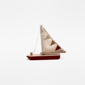 May include: A small wooden sailboat with a red hull and a white sail with brown and red triangular flags. The sailboat is a toy.