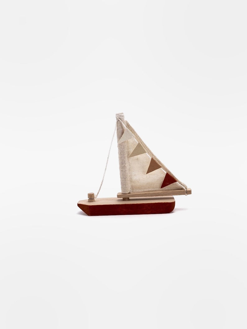 May include: A small wooden sailboat with a red hull and a white sail with brown and red triangular flags. The sailboat is a toy.