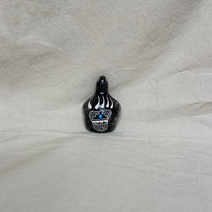 May include: Black and white ceramic bear paw figurine with a turquoise stone inlay. The figurine is hand-painted and has a textured surface.