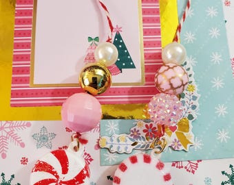 May include: A festive Christmas-themed ornament featuring a red and white striped candy cane and a white peppermint candy. The ornament is adorned with pink, gold, and pearl beads, and is set against a backdrop of pink and blue snowflake patterns.