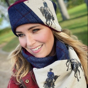 May include: A woman wearing a navy blue and burgundy plaid headband with a white background and a horse rider design. She is also wearing a matching scarf with a similar design.
