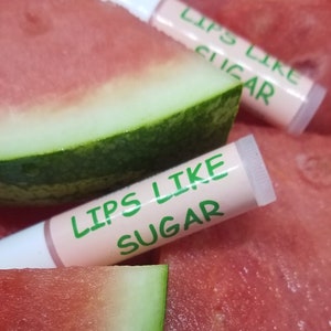 May include: Two pink lip balm tubes with the text "Lips Like Sugar" in green letters on a background of watermelon slices.