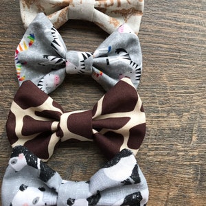 May include: Four fabric bow ties with different animal prints. The top bow tie is beige with brown elephants, the second is gray with black and white zebras, the third is brown with a tan giraffe print, and the bottom is gray with black and white pandas.