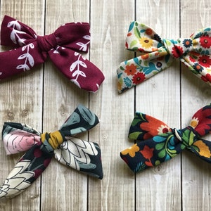 May include: Four fabric hair bows with different floral patterns. The bows are in shades of red, green, blue, yellow, and white.