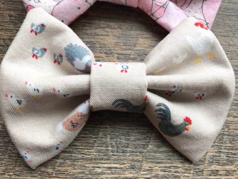 May include: A beige bow tie with a white and gray chicken print. The bow tie is made of fabric and has a simple design.