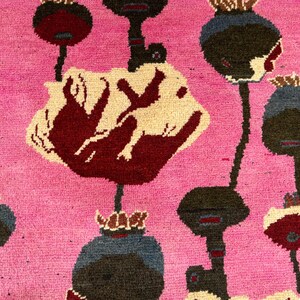 K&ouml;nnte beinhalten: Nahaufnahme eines pinkfarbenen Teppichs mit einem sich wiederholenden Muster aus stilisierten Blumenformen. Die Blumen sind in Burgunder-, Creme-, Schwarz- und Blaut&ouml;nen gehalten. Der Teppich hat ein strukturiertes, gewebtes Aussehen.