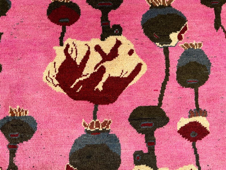 K&ouml;nnte beinhalten: Nahaufnahme eines pinkfarbenen Teppichs mit einem sich wiederholenden Muster aus stilisierten Blumenformen. Die Blumen sind in Burgunder-, Creme-, Schwarz- und Blaut&ouml;nen gehalten. Der Teppich hat ein strukturiertes, gewebtes Aussehen.