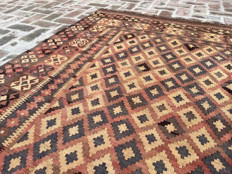 K&ouml;nnte beinhalten: Ein Vintage-Teppich mit einem geometrischen Muster in Braun-, Beige- und Rott&ouml;nen. Der Teppich hat einen abgenutzten und verblassten Look, der ihm ein rustikales und antikes Aussehen verleiht.