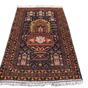 May include: A rectangular area rug featuring a dark navy blue background with a central urn motif in shades of red, gold, and cream. The design includes geometric borders, stylized floral patterns, and white fringe along the top and bottom edges.