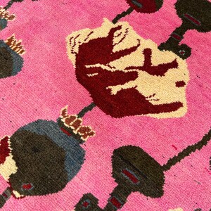K&ouml;nnte beinhalten: Nahaufnahme eines pinkfarbenen Teppichs mit floralem Muster. Der Teppich zeigt gro&szlig;e, stilisierte Blumen in Burgunder, Creme und Grau, vor einem leuchtend pinkfarbenen Hintergrund. Das Design hat ein strukturiertes, gewebtes Aussehen.