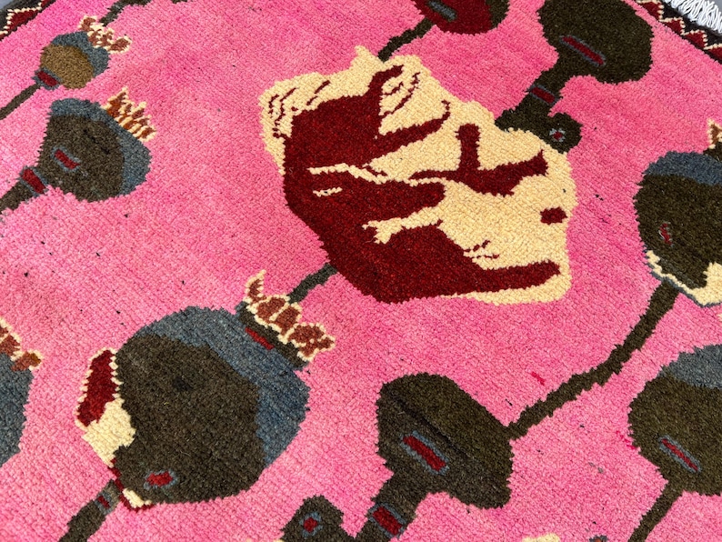 K&ouml;nnte beinhalten: Nahaufnahme eines pinkfarbenen Teppichs mit floralem Muster. Der Teppich zeigt gro&szlig;e, stilisierte Blumen in Burgunder, Creme und Grau, vor einem leuchtend pinkfarbenen Hintergrund. Das Design hat ein strukturiertes, gewebtes Aussehen.