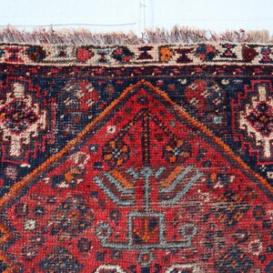 Pu&ograve; includere: Un tappeto persiano vintage con uno schema di colori rosso, blu e crema. Il tappeto ha una forma di diamante centrale con intricati motivi floreali e un bordo con disegni geometrici.