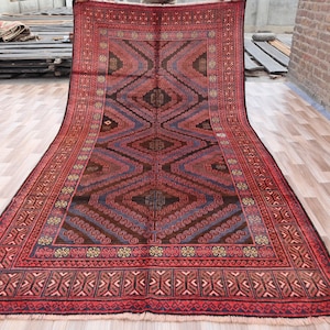 Pode incluir: Um tapete persa tradicional com um esquema de cores vermelho, azul e castanho. O tapete tem um padrão geométrico com uma forma de diamante central e uma borda de desenhos florais intrincados.