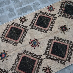 May include: A beige rug with a geometric pattern of black diamonds and star shapes in shades of red, pink, blue, and brown.