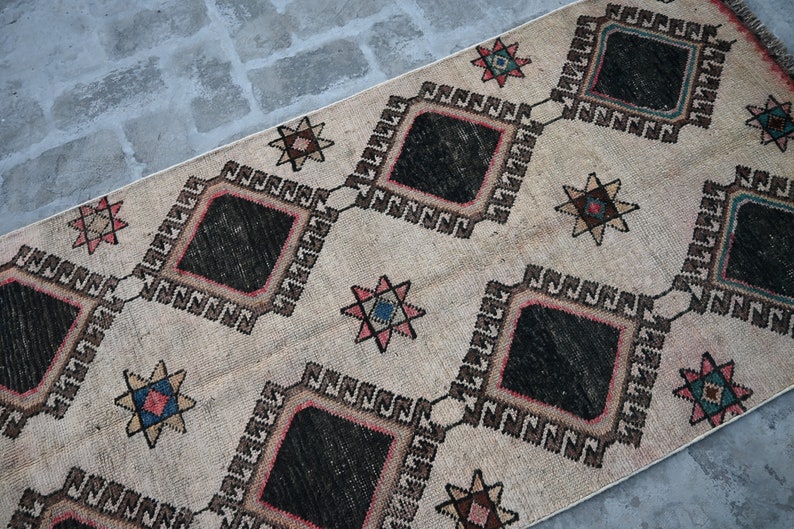 May include: A beige rug with a geometric pattern of black diamonds and star shapes in shades of red, pink, blue, and brown.