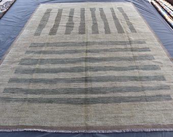 Op de afbeelding: Een rechthoekig vloerkleed met een neutrale beige achtergrond en grijze horizontale en verticale streepmotieven. Het vloerkleed heeft een franje aan de onderkant. Het vloerkleed is gemaakt van een geweven materiaal.