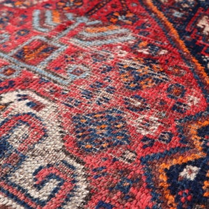 Pu&ograve; includere: Primo piano di un tappeto colorato con motivi intricati in tonalit&agrave; di rosso, blu, arancione e bianco. Il tappeto ha una superficie testurizzata e tessuta.