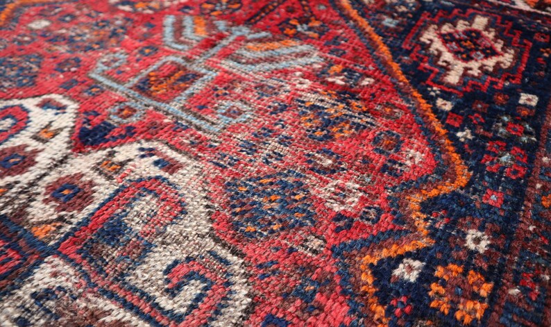 Pu&ograve; includere: Primo piano di un tappeto colorato con motivi intricati in tonalit&agrave; di rosso, blu, arancione e bianco. Il tappeto ha una superficie testurizzata e tessuta.