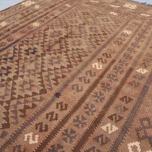 K&ouml;nnte beinhalten: Ein brauner und beigefarbener Teppich mit geometrischem Muster. Der Teppich hat ein traditionelles Aussehen und ist aus Wolle.