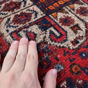 Pu&ograve; includere: Primo piano di un tappeto rosso, blu e bianco con un motivo con una mano appoggiata sulla superficie.
