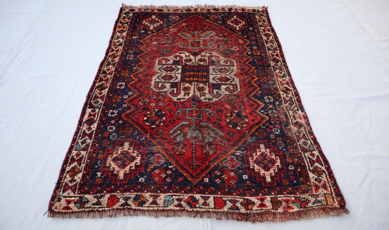 Pu&ograve; includere: Un tappeto rosso, blu e crema con un design persiano tradizionale. Il tappeto ha un bordo a frangia ed &egrave; fatto di lana.