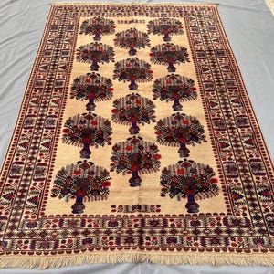 May include: A rectangular beige rug with a repeating pattern of stylized trees in vases. The trees have red and blue floral designs. The rug has a red and blue border with a fringe.