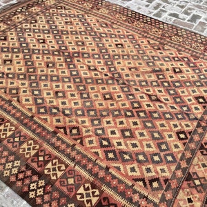 K&ouml;nnte beinhalten: Ein Vintage-Teppich mit einem geometrischen Muster in Rot-, Braun- und Beiget&ouml;nen. Der Teppich hat ein Rautenmuster in der Mitte und einen Rand mit einem komplizierteren Design.