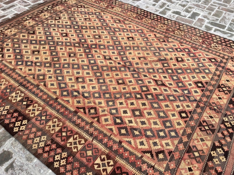 K&ouml;nnte beinhalten: Ein Vintage-Teppich mit einem geometrischen Muster in Rot-, Braun- und Beiget&ouml;nen. Der Teppich hat ein Rautenmuster in der Mitte und einen Rand mit einem komplizierteren Design.