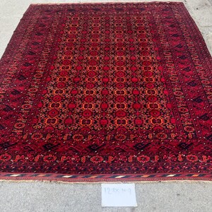 May include: A large, rectangular red rug with an intricate, repeating floral pattern in shades of red, orange, and black. The rug has a detailed border and a central design. The rug measures 12 x 9 feet.