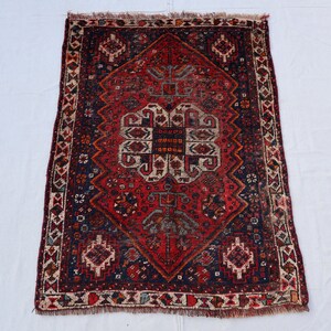Pu&ograve; includere: Un tappeto rosso, blu e crema con un design persiano tradizionale. Il tappeto ha un centro a forma di diamante con intricati motivi floreali e un bordo di forme geometriche ripetute.