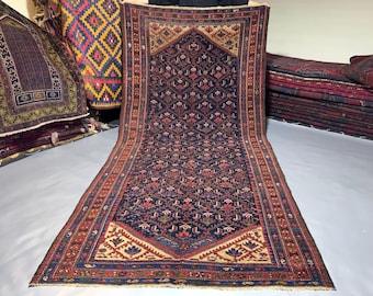 May include: A rectangular area rug featuring a dark blue central field with a repeating geometric floral pattern in red, cream, and light blue. The rug has a pointed arch design at the top and bottom, framed by a wide border with intricate motifs.