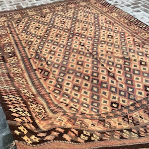 K&ouml;nnte beinhalten: Ein brauner und beiger Teppich mit einem Rautenmuster. Der Teppich hat einen dunkelbraunen Rand mit komplizierten Mustern.