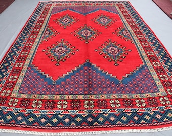 Puede incluir: Una alfombra roja con un patrón geométrico azul y blanco. La alfombra tiene un borde de flecos.