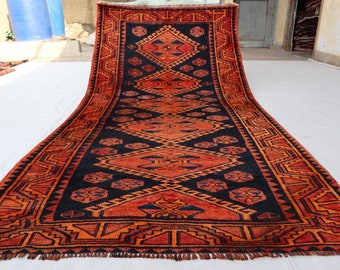 Puede incluir: Una alfombra larga y estrecha con un patrón geométrico en tonos rojos, naranjas y negros. La alfombra tiene flecos en ambos extremos.
