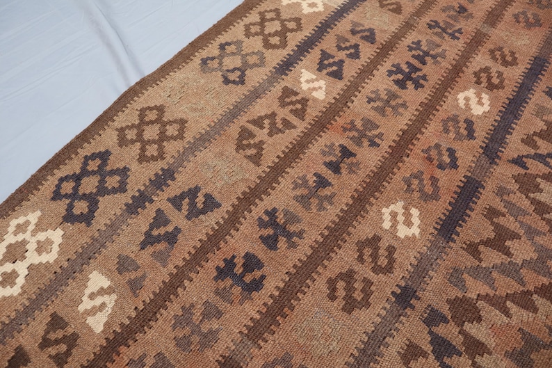 K&ouml;nnte beinhalten: Ein brauner und beigefarbener Teppich mit geometrischen Mustern. Der Teppich hat eine traditionelle gewebte Textur.