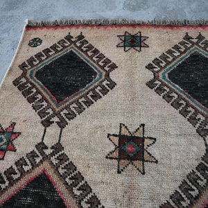 May include: A cream-colored rug with a geometric pattern in black, brown, red, and blue. The pattern features repeating diamond shapes and star-like designs.