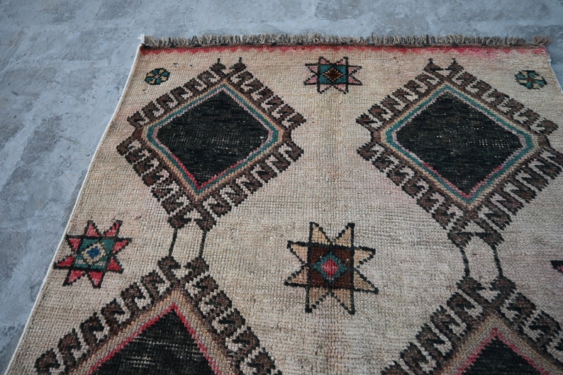 May include: A cream-colored rug with a geometric pattern in black, brown, red, and blue. The pattern features repeating diamond shapes and star-like designs.