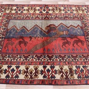 Op de afbeelding: Een traditioneel tapijt met een crèmekleurige achtergrond en een geometrisch patroon in rood, blauw en bruin. Het midden van het tapijt toont een gestileerde berg scène met een rood, blauw en bruin ontwerp.