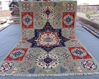 Può includere: Un grande tappeto rettangolare con sfondo verde salvia e intricati motivi geometrici in rosso, blu navy e bianco. Il tappeto presenta un motivo a medaglione centrale e bordi decorativi.