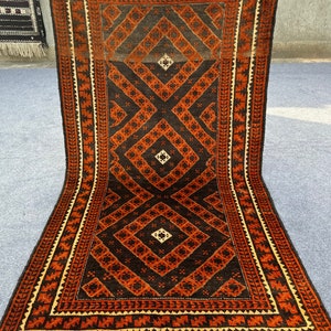 Pode incluir: Um tapete tradicional com um padrão geométrico preto, laranja e creme. O tapete tem uma borda de franjas.