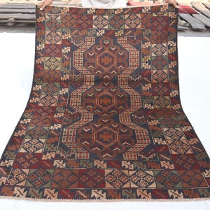 May include: A rectangular area rug featuring a dark blue central field with three repeating geometric medallions in rust orange and brown. The border displays a complex pattern of squares containing smaller geometric motifs in red, green, and tan.