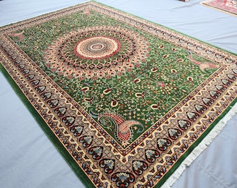 Può includere: Un tappeto rettangolare verde con un intricato disegno floreale. Il tappeto presenta un medaglione centrale con accenti rossi e crema, circondato da un bordo dettagliato con motivi paisley e floreali. Il tappeto ha una frangia sui bordi.