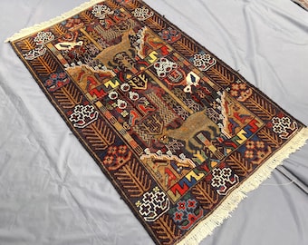 Puede incluir: Una alfombra tejida rectangular con fondo azul oscuro y dos figuras de ciervos de color tostado en el centro. El diseño incluye patrones geométricos, árboles estilizados y motivos florales en rojo, amarillo y blanco. Tiene flecos blancos en los extremos.